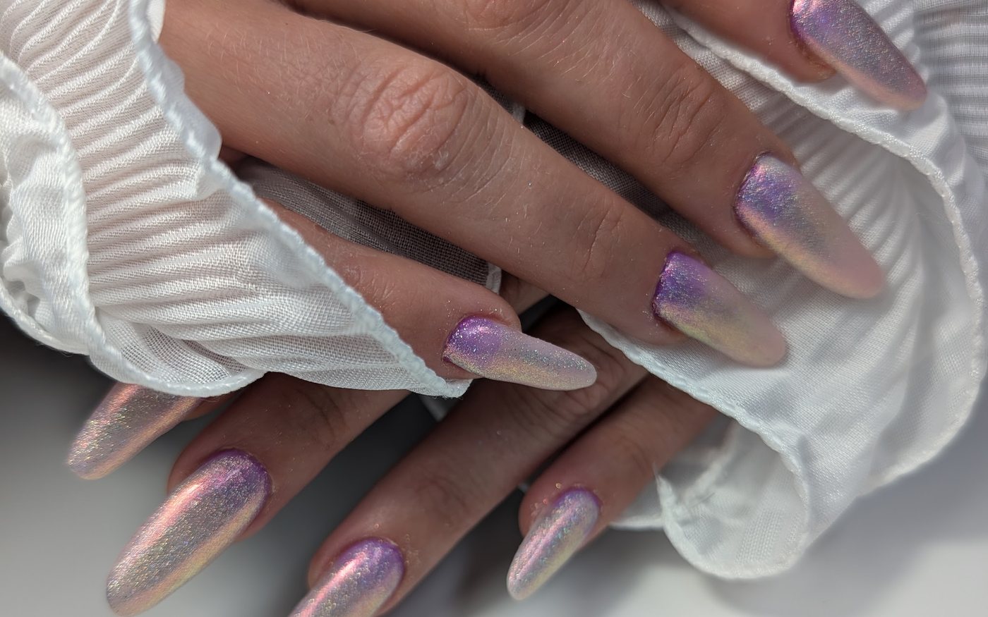 Lange amandelvormige nagels met een roze en lila chrome-glans op een witte ruche-mouw