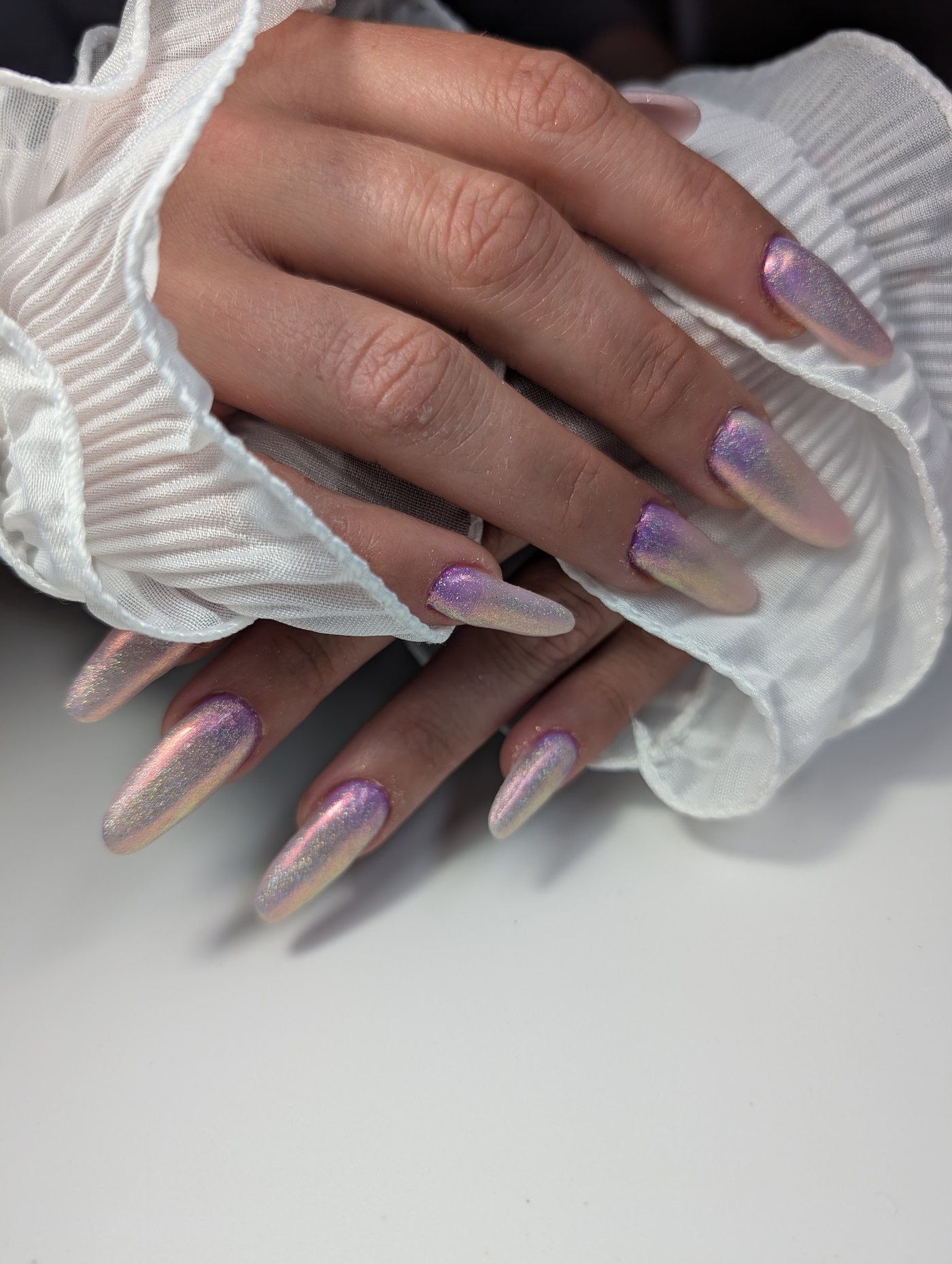 Lange amandelvormige nagels met een roze en lila chrome-glans op een witte ruche-mouw