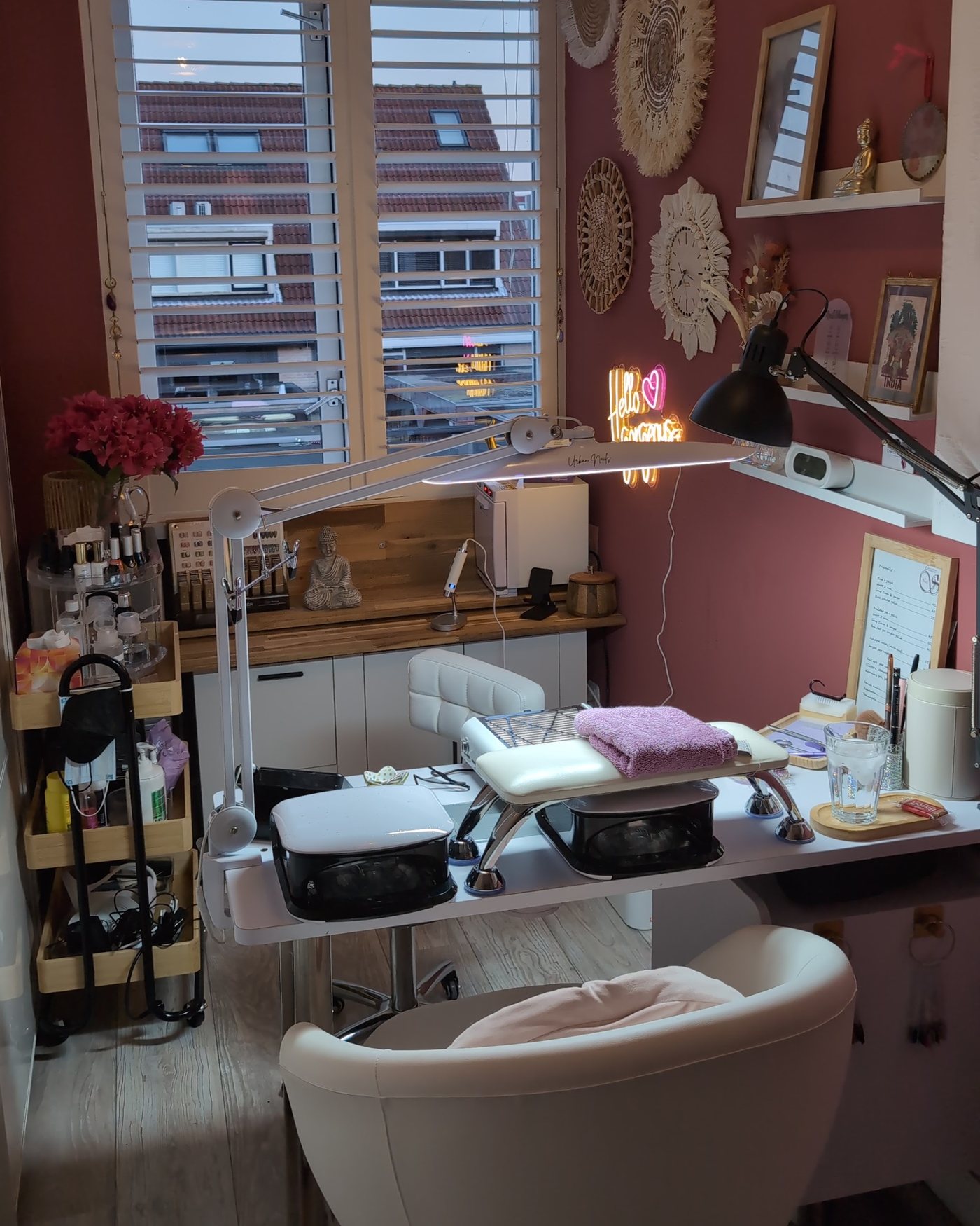 De nageltafel met twee lampen, een roze handdoek op de handsteun, witte stoel en macramé aan de muur